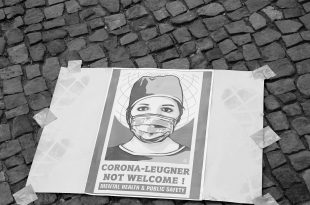 Auf dem Gehweg liegendes Plakat auf dem eine mundschutz tragende Person gezeigt wird. Darunter der Slogan: Corona-Leugner not welcome