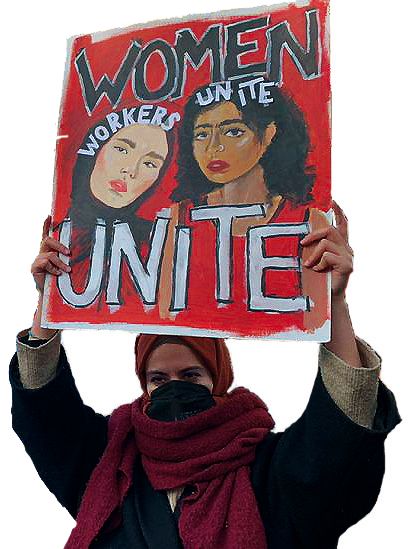 Eine Schwarze Frau hält ein Schild bei einer Demonstration hoch. Sie trägt einen Schal und ein Kopftuch. Auf dem Schild steht als Überschrift WOMEN und am Ende des Kartons UNITE. Weiter ist darauf eine weiße Frau mit Kopftuch gemalt über ihrem Kopf steht WORKERS und neben ihr ist eine schwarze Frau mit offenen Haaren gezeichnet, über ihrem Kopf steht UNITE.